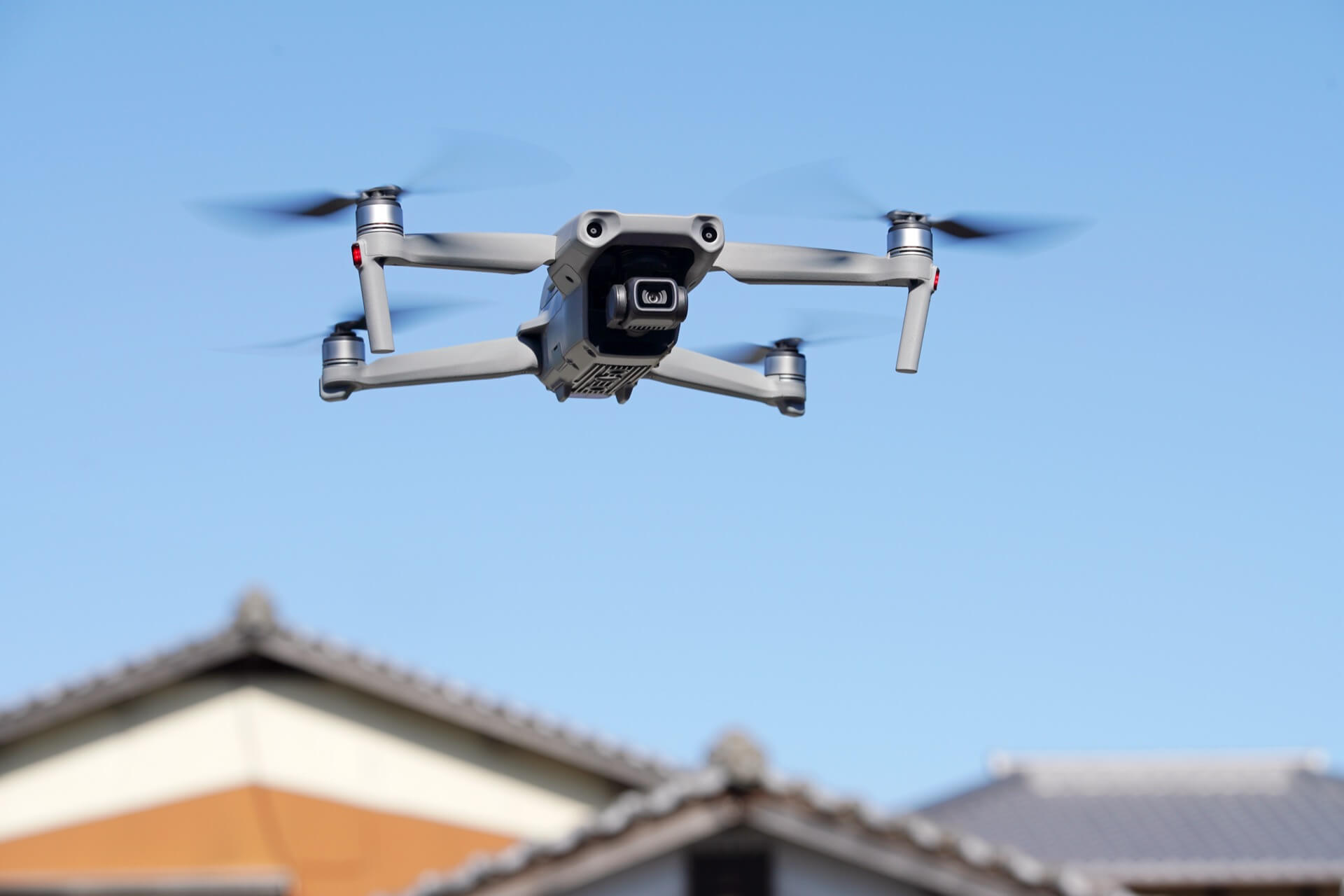 住宅の屋根の上空でホバリングする撮影用ドローン