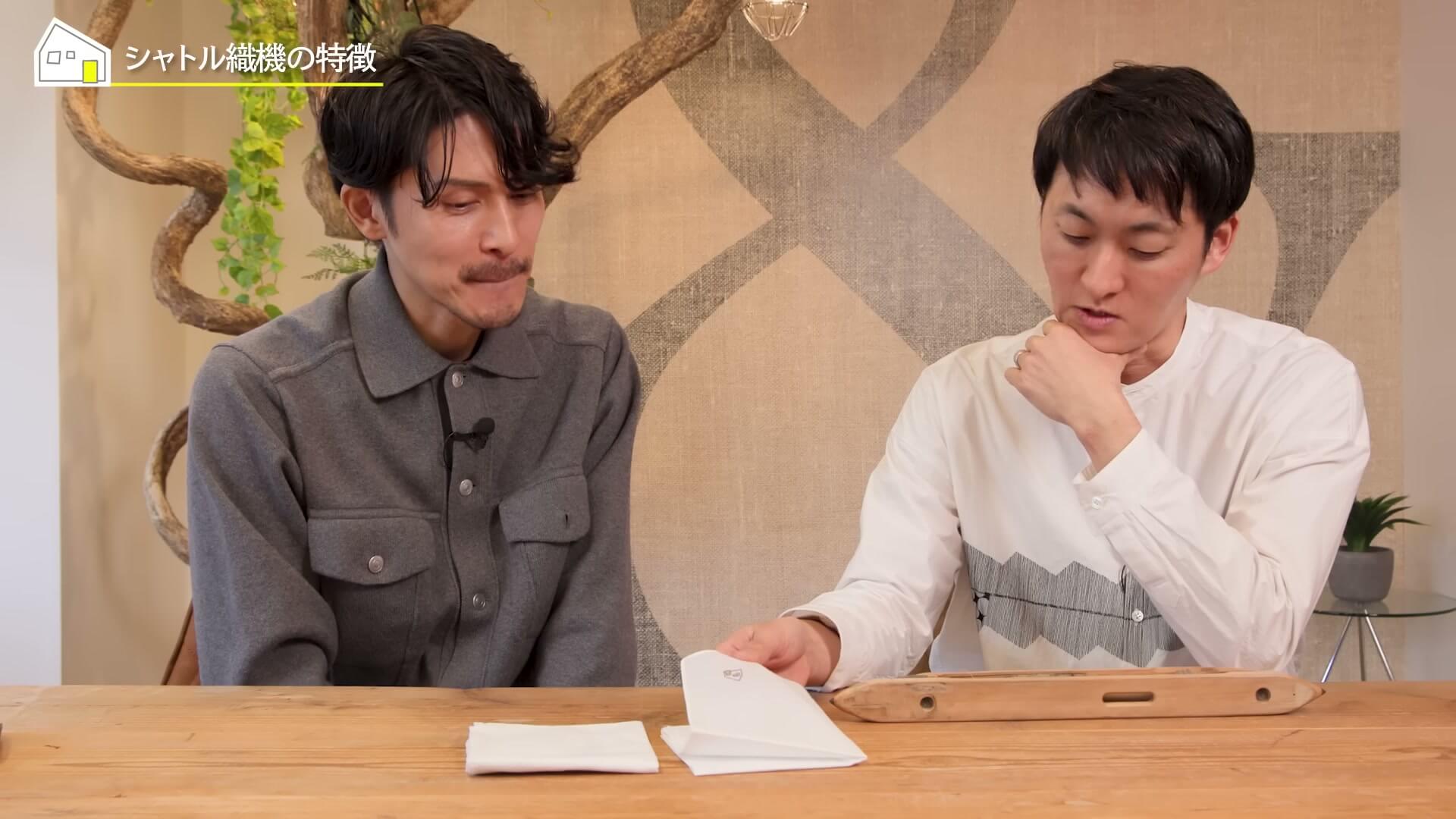 テーブルの上の生地見本を手に取って話す松下さんと中村