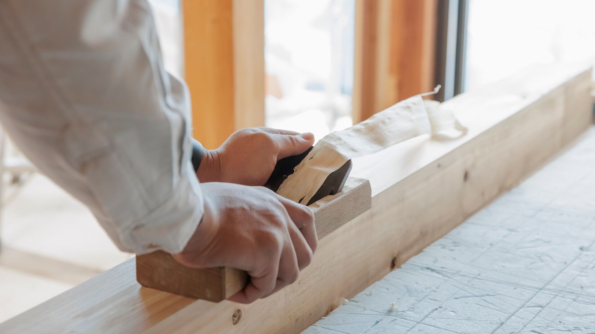 窓から自然光が入る作業場で、角材に鉋をかける職人の手元