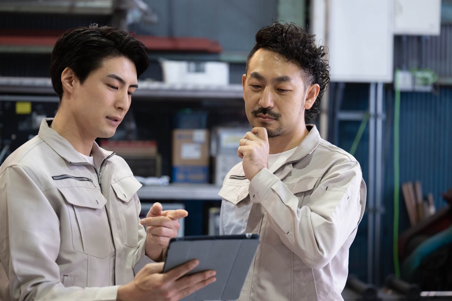 工場で、タブレットの画面を見ながら作業手順を確認する2人の作業員