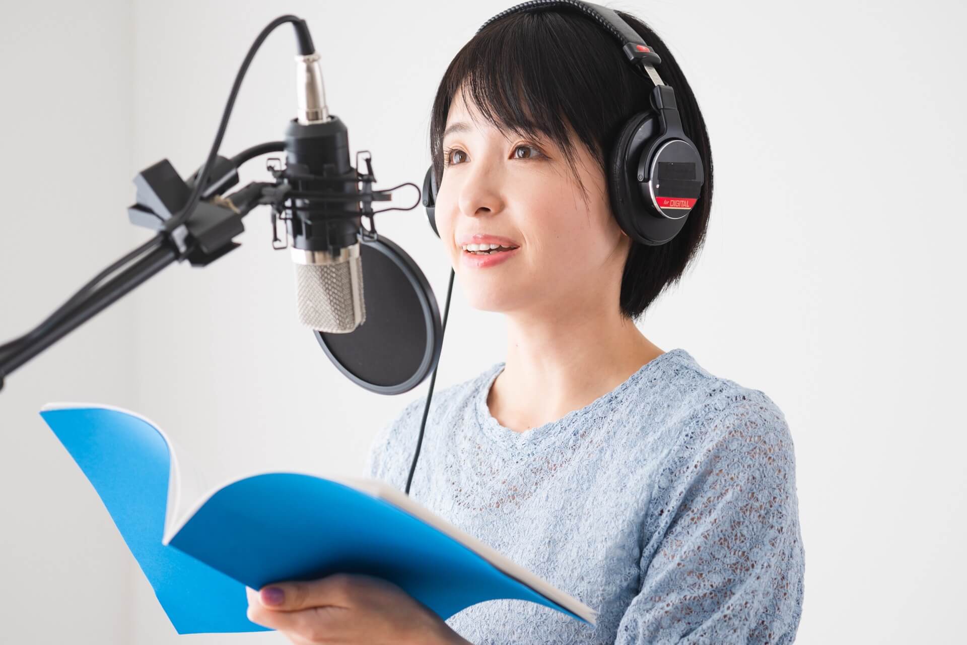 ヘッドホンを着けて台本を持ち、マイクの前でナレーションを読む女性