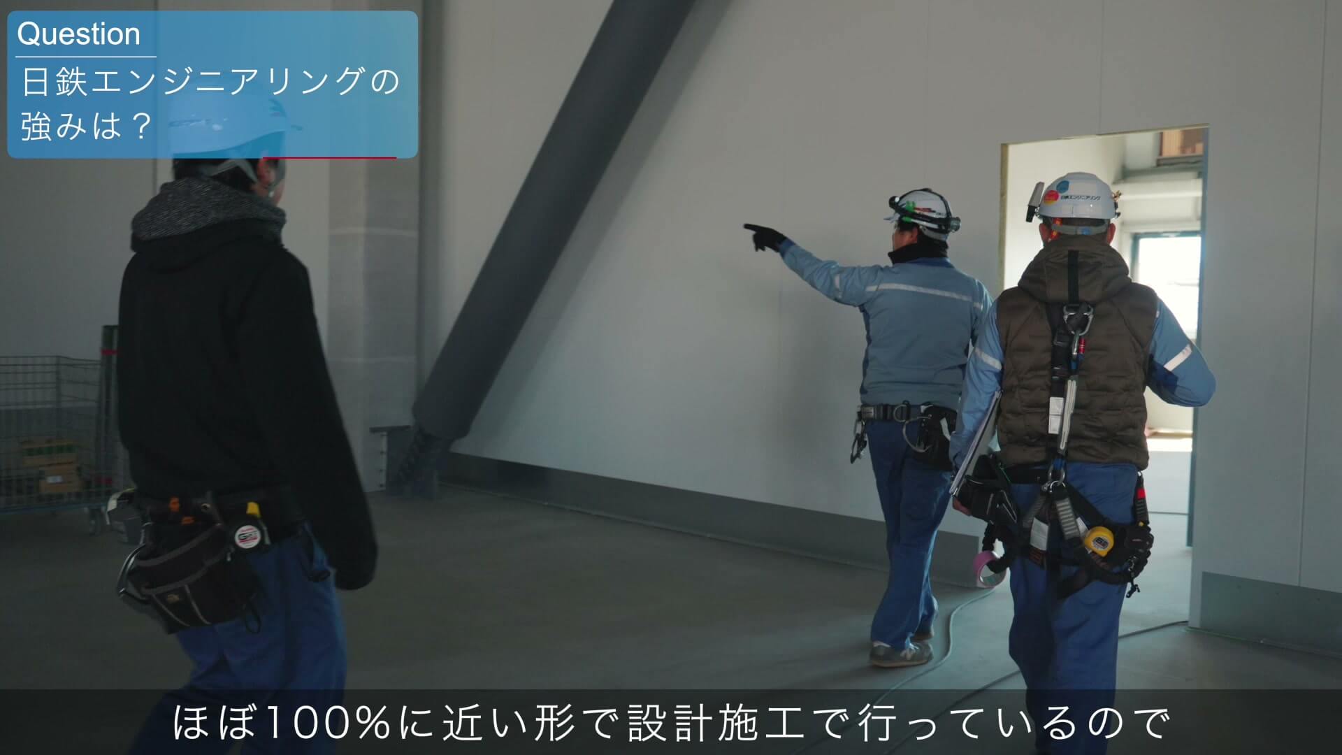 建設中の建物の中で、壁を指さしながら確認するヘルメット姿の社員の後ろ姿