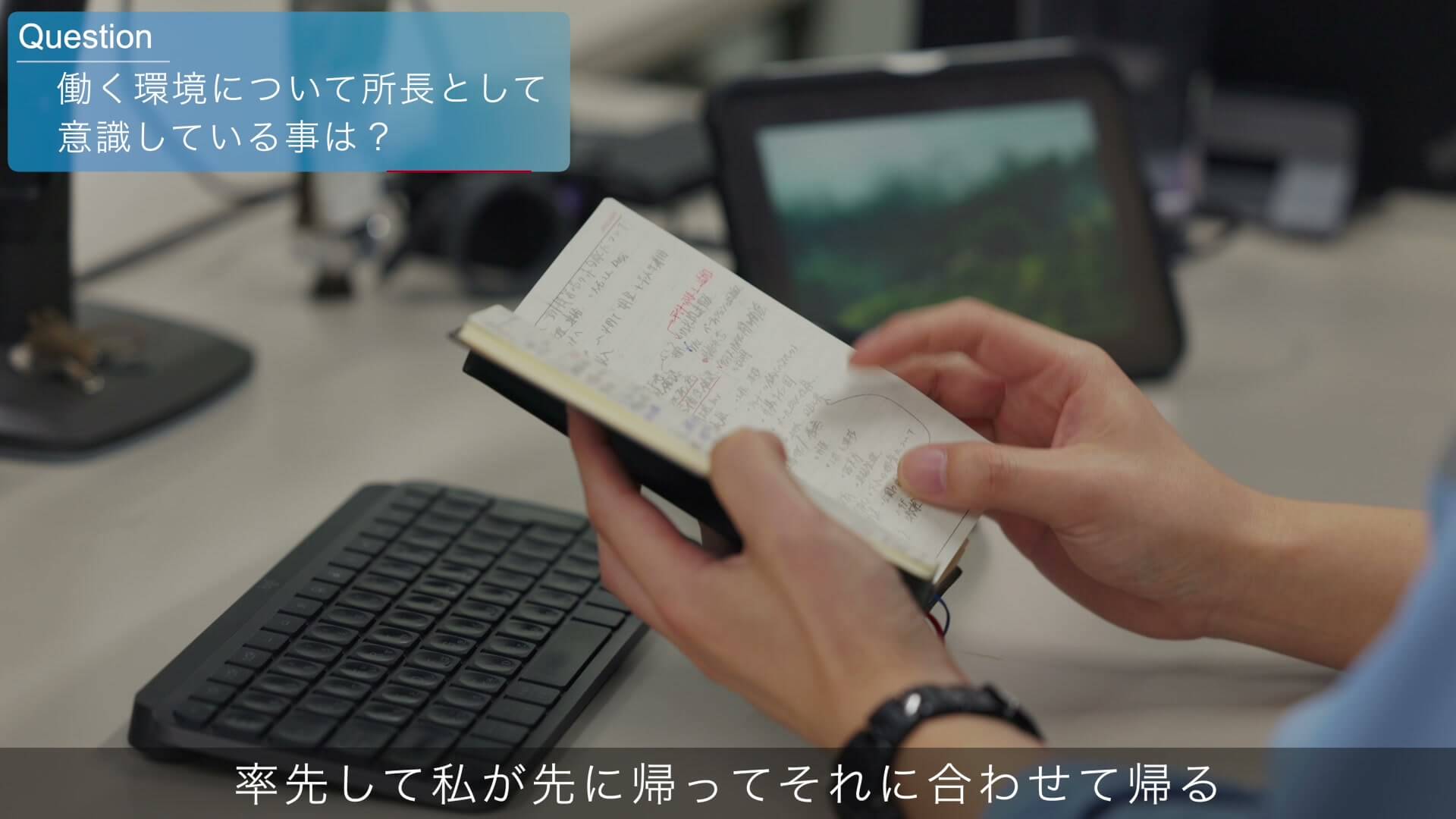 手帳のメモを見ながらキーボードに手を置く現場事務所の様子