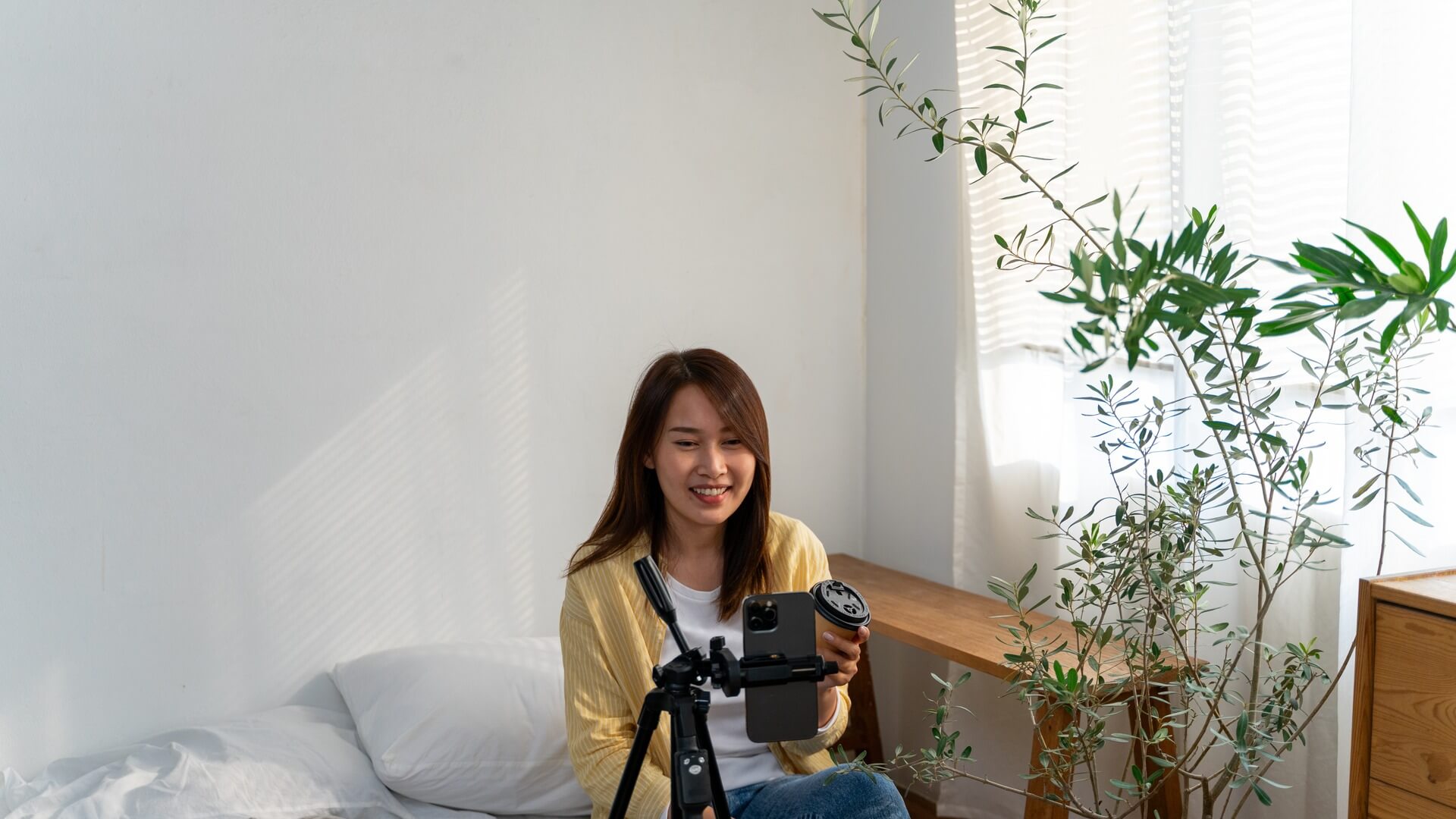 自然光の差し込む部屋で、三脚に立てたスマートフォンに向かって話す女性