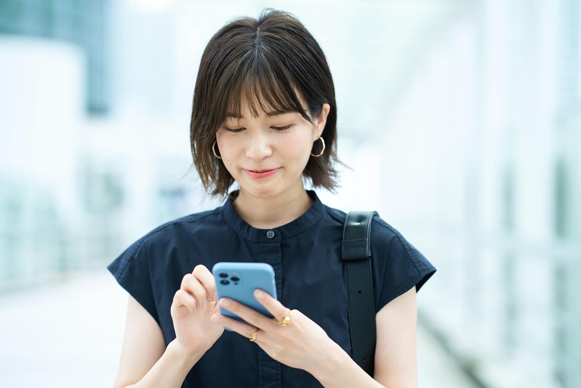 明るい屋外でスマートフォンの画面を見る女性