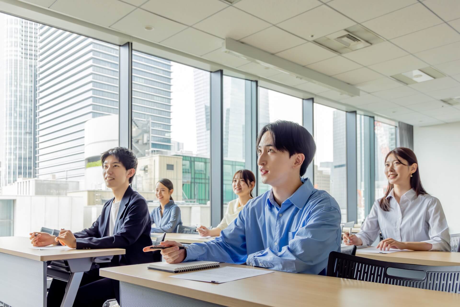 窓の大きな研修室で、講師の話を聞く社員たち