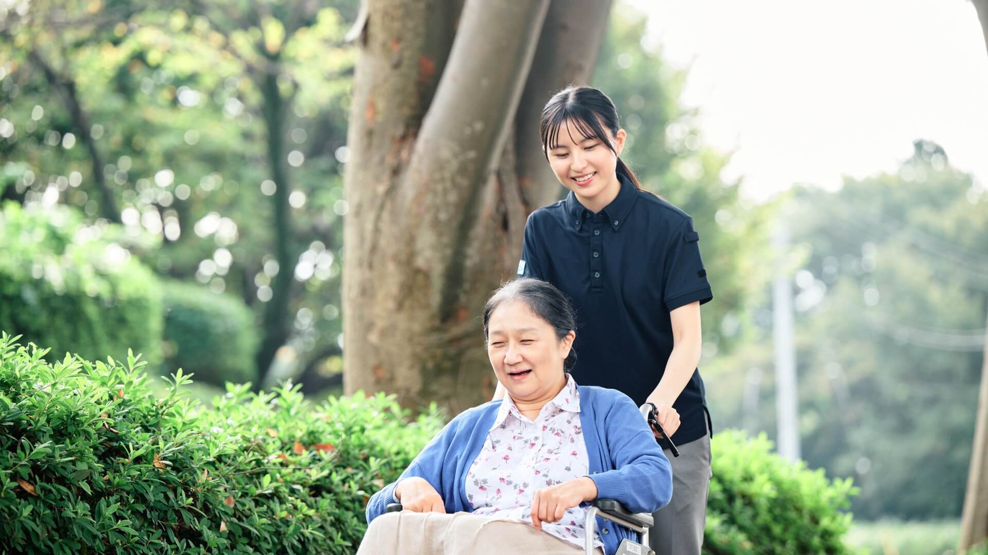 並木道で車椅子を押すスタッフと笑顔のご入居者