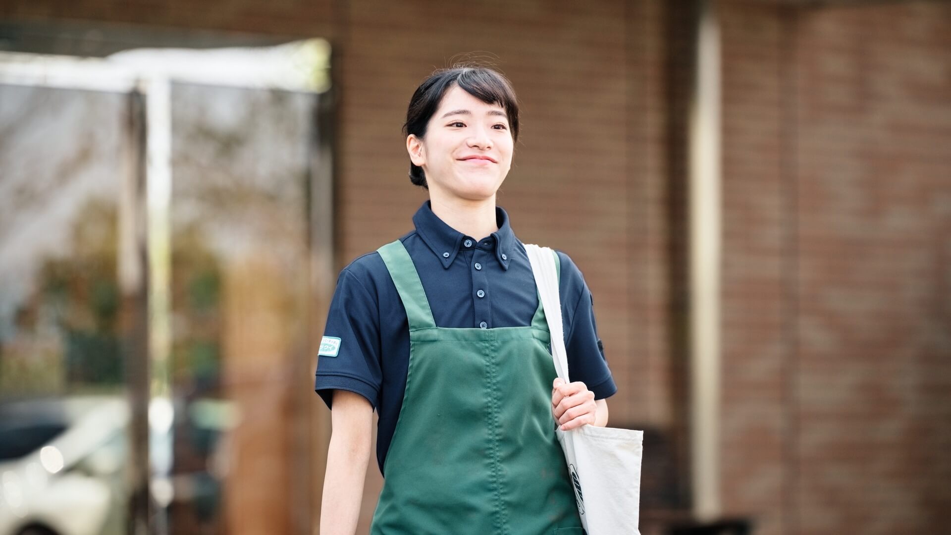 新しいユニフォームのエプロン姿でエントランスを歩くスタッフ