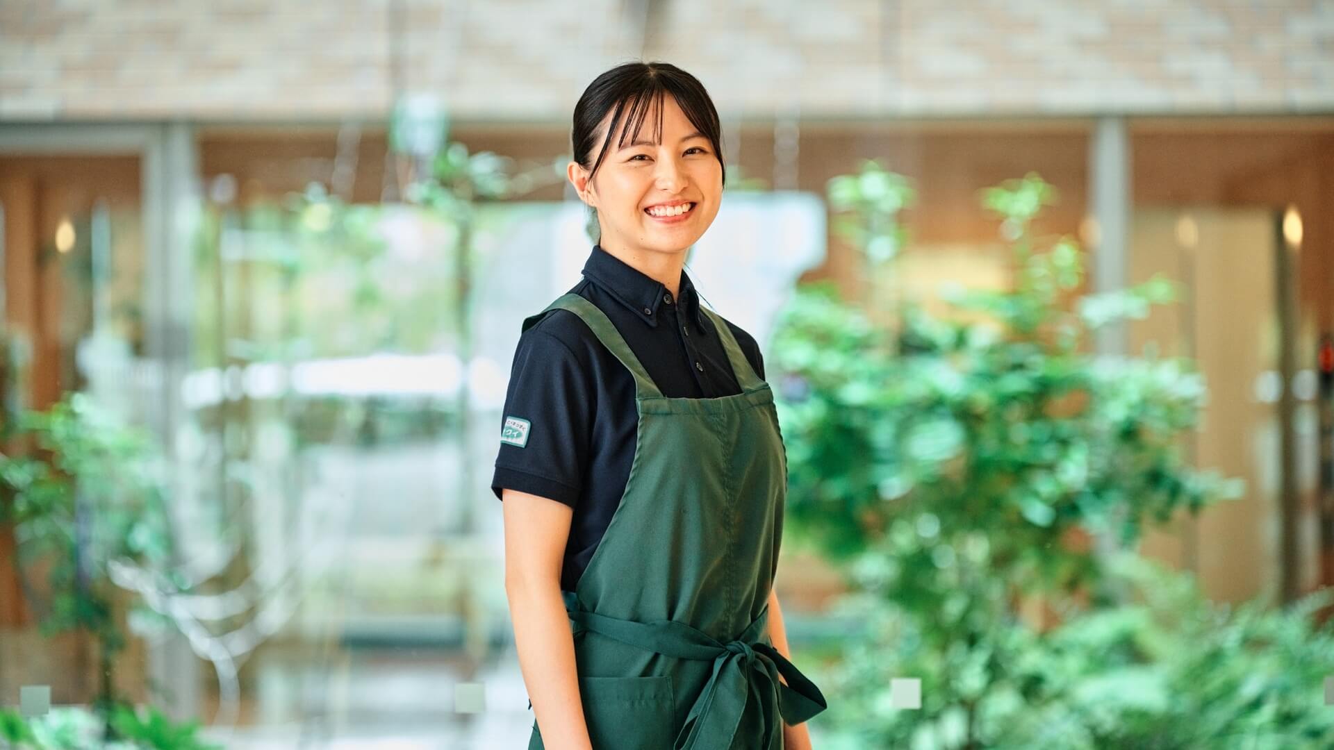植栽のあるロビーで微笑むエプロン姿のスタッフ