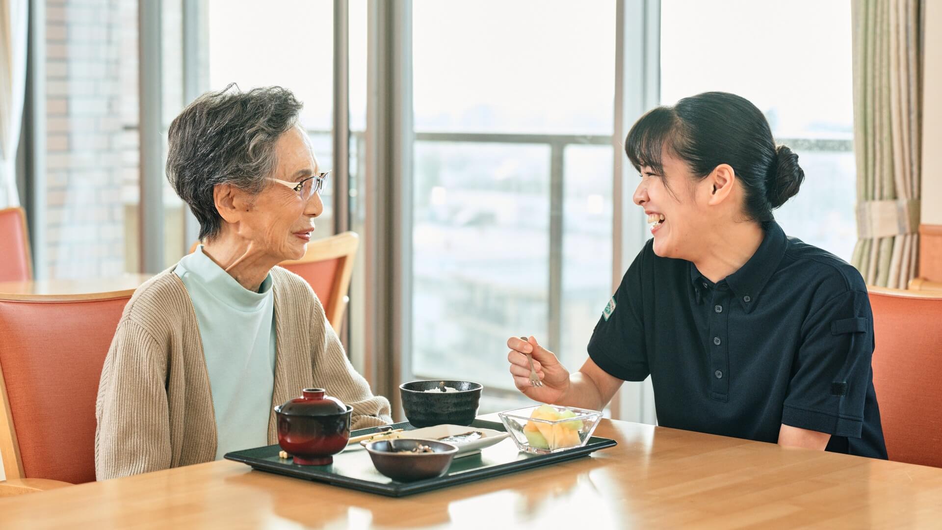 ダイニングで食事をしながらご入居者と言葉を交わすスタッフ