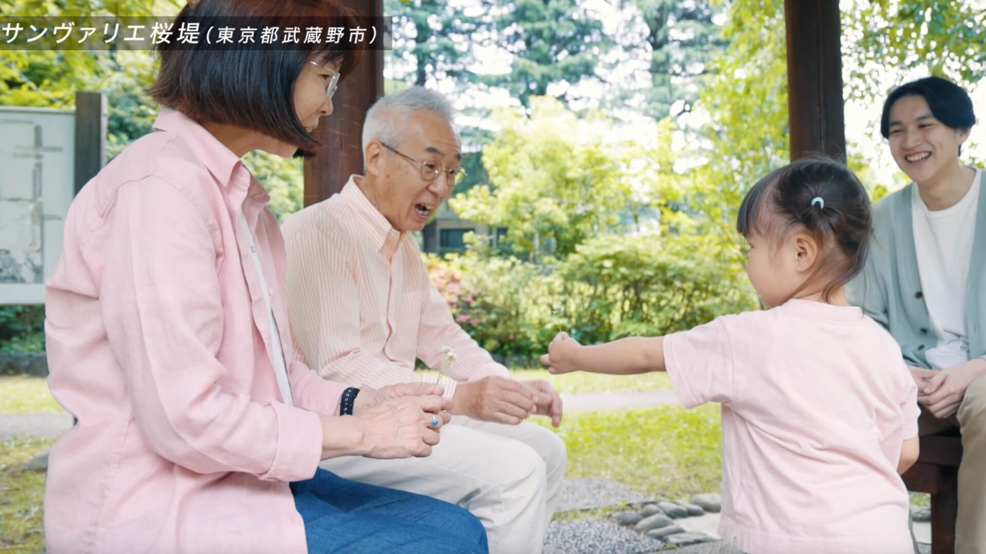 東屋で、シニア夫婦と小さな女の子が手を取り合う場面