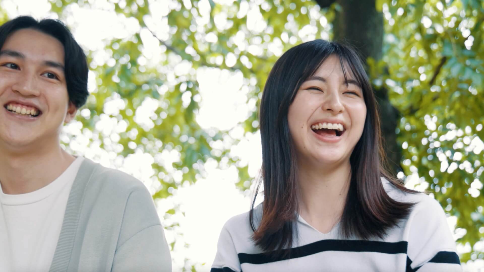 木漏れ日の下で、顔を見合わせて笑う若い夫婦