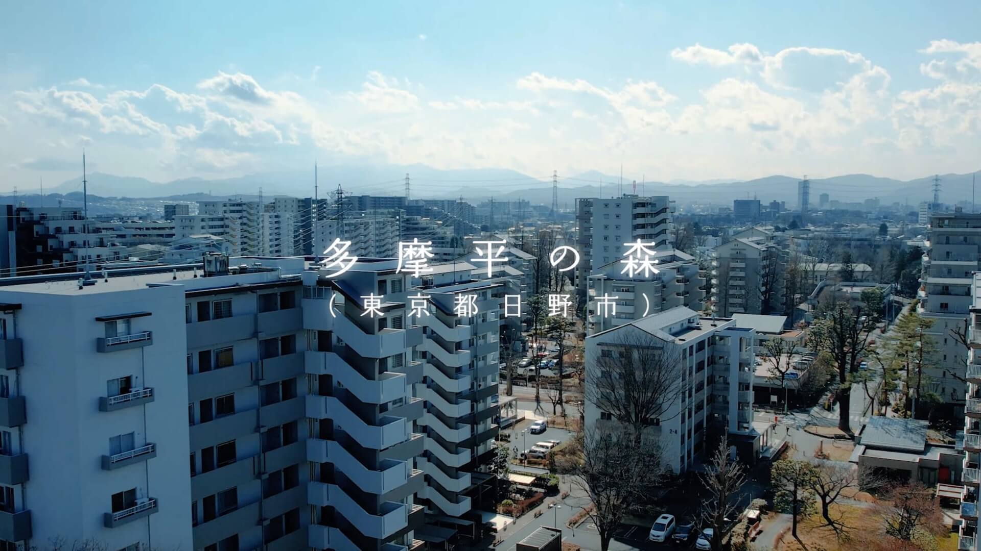 多摩平の森を高い位置から見渡したカットに、団地名と所在地のテロップを入れた場面