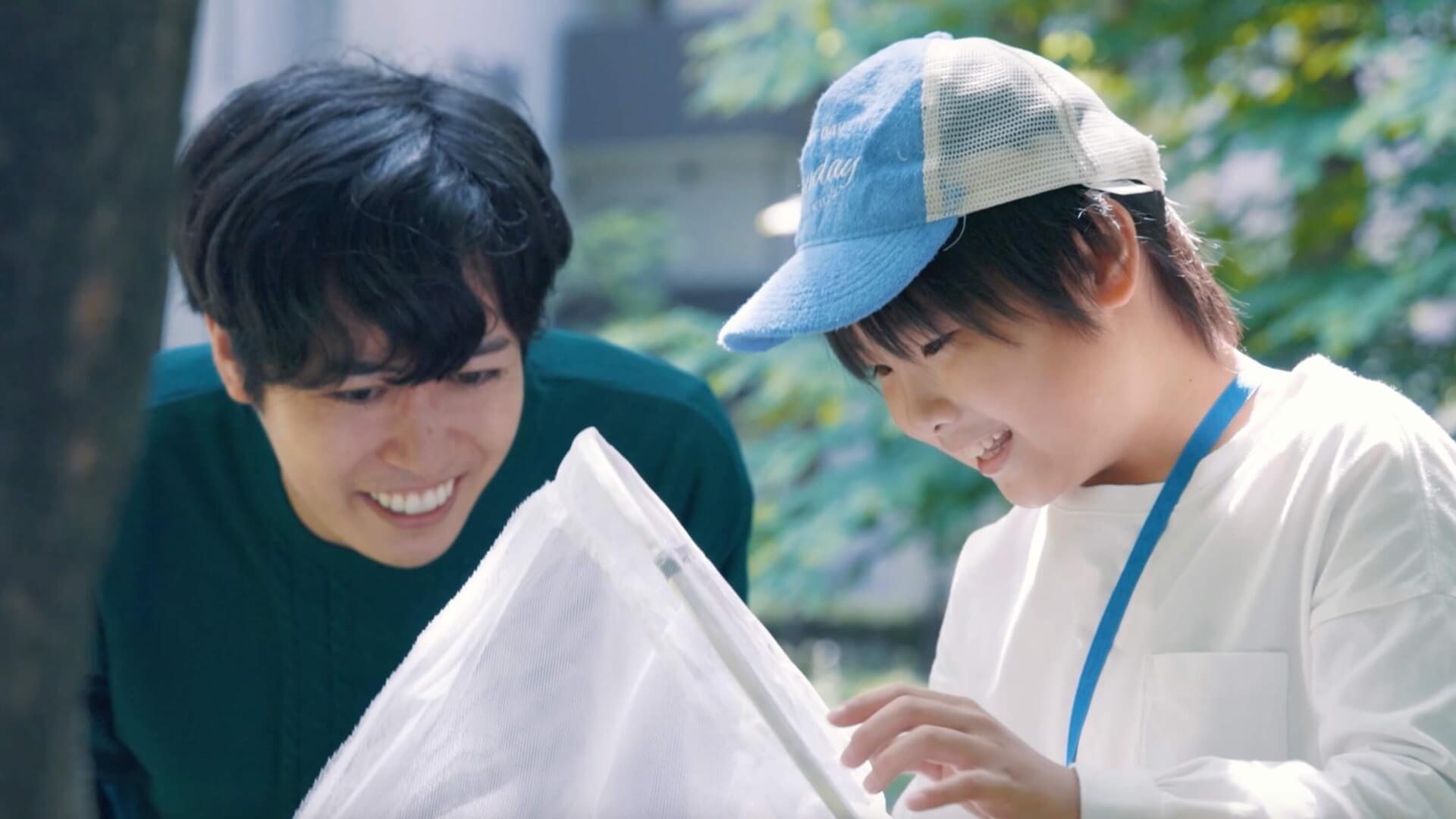 虫取り網の中をのぞき込んで笑う父親と、帽子をかぶった男の子