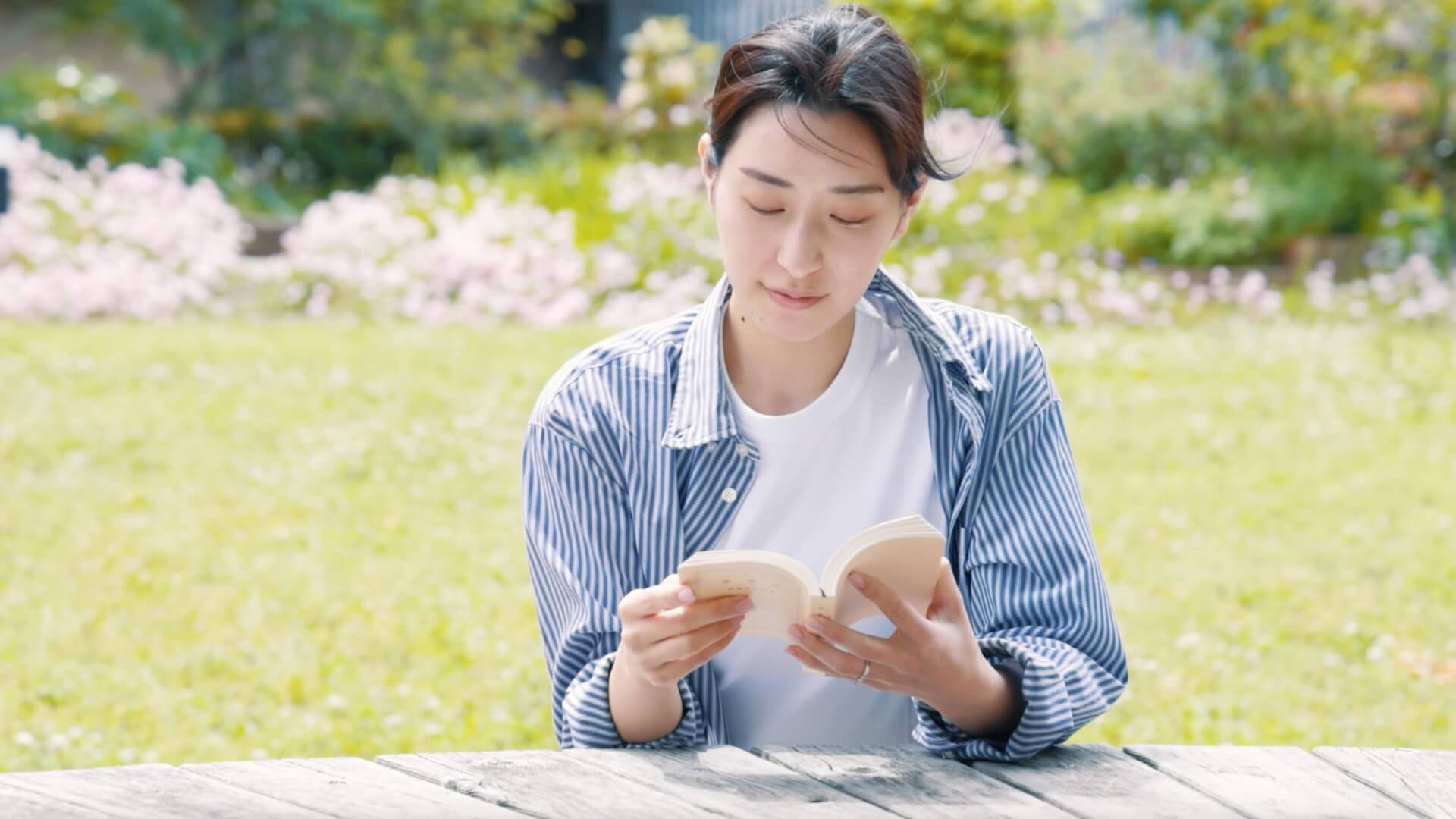 花の咲く芝生の広場で、木のテーブルに本を広げて読む女性