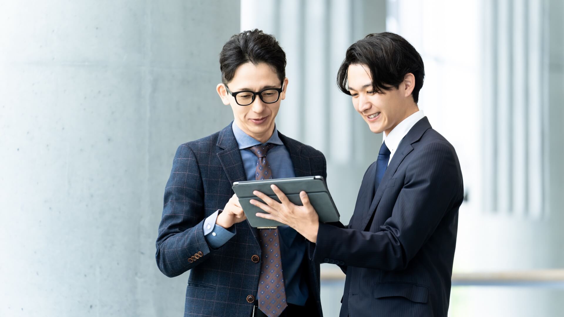 明るいオフィスで、タブレットの画面を一緒に確認する2人のビジネスマン